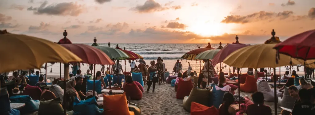 Seminyak Beach in Bali with soft golden sand, gentle waves, colorful umbrellas, and people relaxing or walking by the shore.