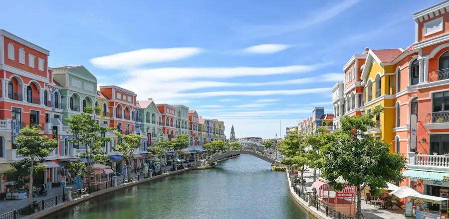 Colorful buildings lining the riverbank in Phu Quoc, Vietnam, reflected in the calm water under a blue sky.