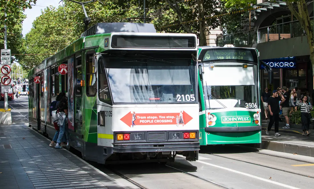 Melbourne trams travel through the city’s central business district, surrounded by modern buildings, busy streets, and pedestrians.