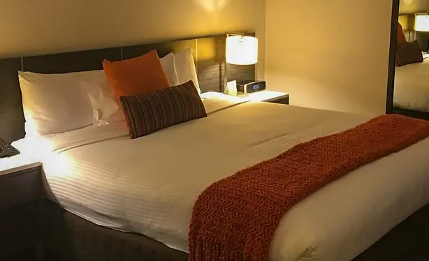 Interior of a Novotel Sydney Airport hotel room, showing a double bed and a bedside table with a lit lamp.