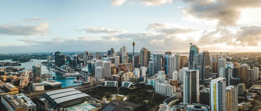 Panoramic view of the Sydney skyline featuring tall buildings and the Sydney Tower against a blue sky.